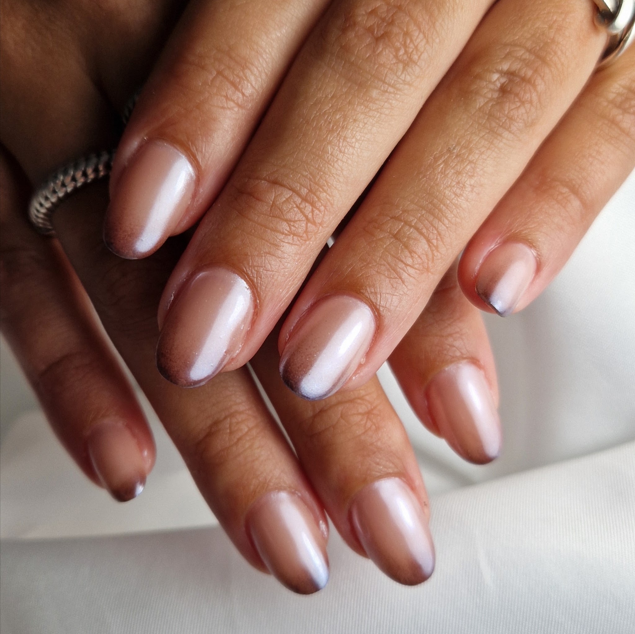 Verzorgde handen met parelmoer nude gelakte amandelnagels op wit satijn