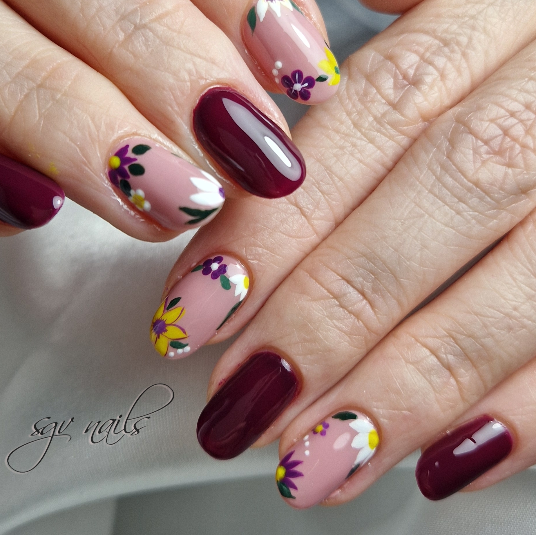 Bordeaux nagels met roze accentnagels vol paarse, gele en witte bloemen